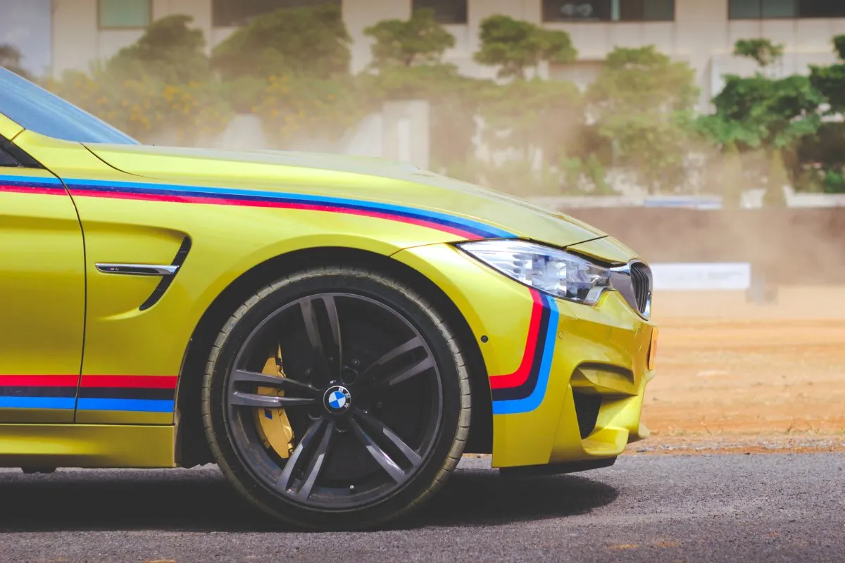 Yellow BMW M4 with racing stripes, side profile