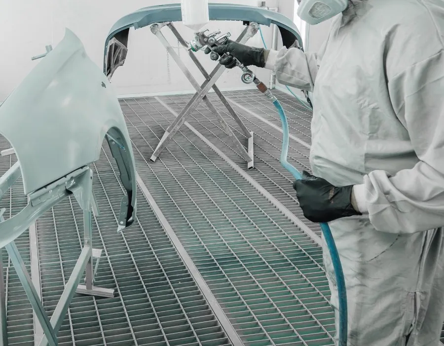 Painter spraying a car bumper in the spray booth