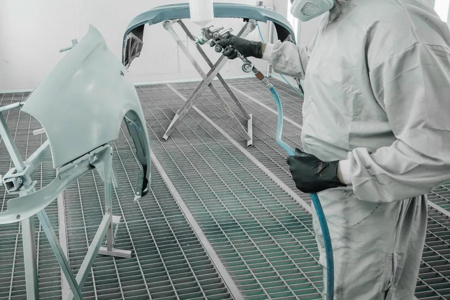 Painter spraying a car bumper in the spray booth