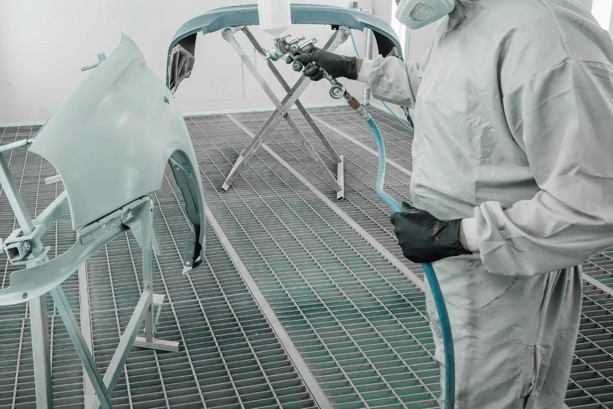 Painter spraying a car bumper in the spray booth